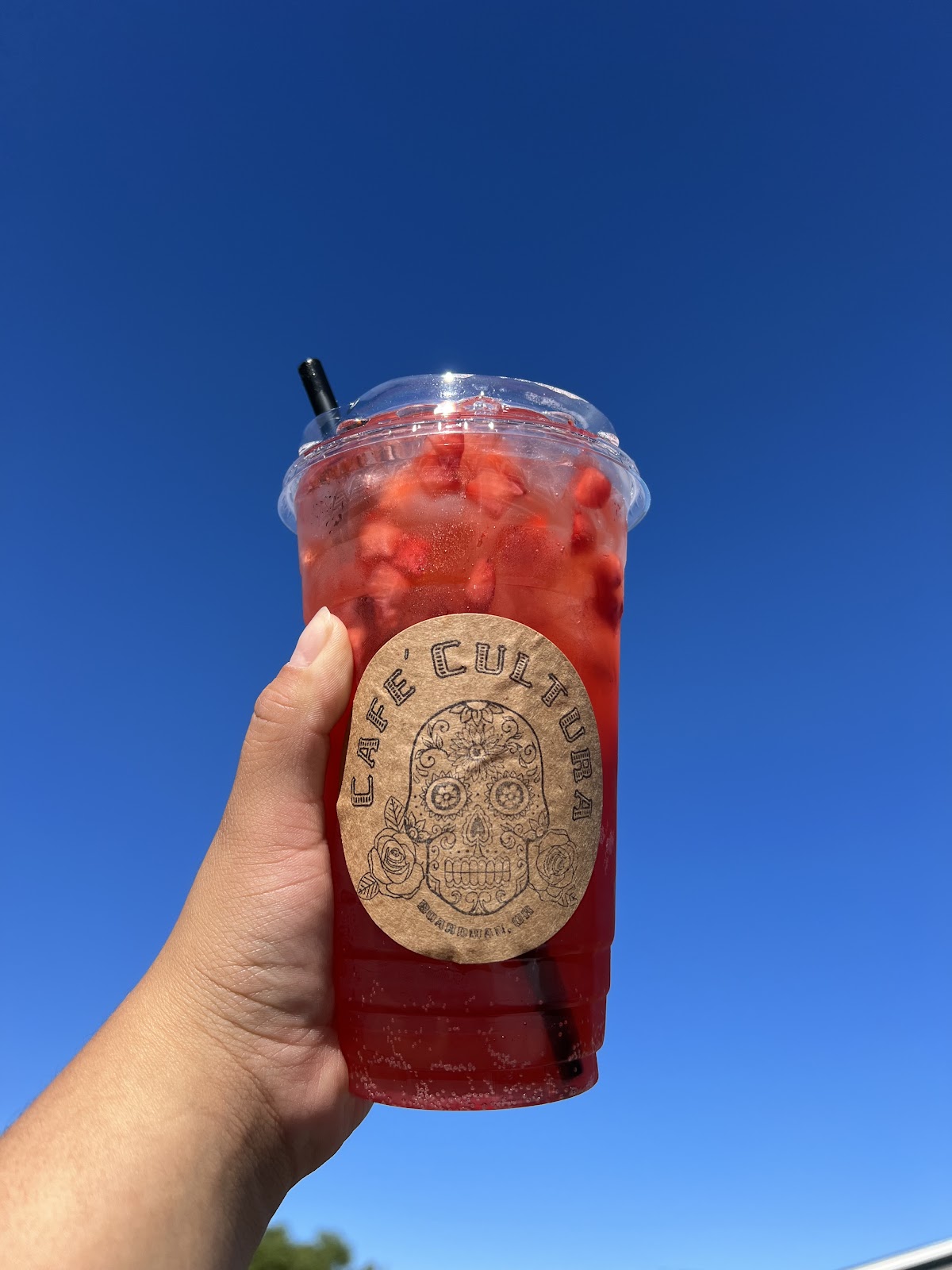 Strawberry refresher with fresh strawberries in a Cafe Cultura cup against a bright sky